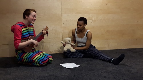 Photo of two people: one with a teddy bear, one strumming a ukulele