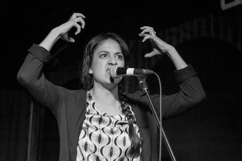 Photo of Jillian Welsh standing at a microphone with her arms raised and her hands imitating claws.
