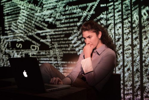 A woman staring at a laptop screen. A mess of internet comments projected on the surface behind her.