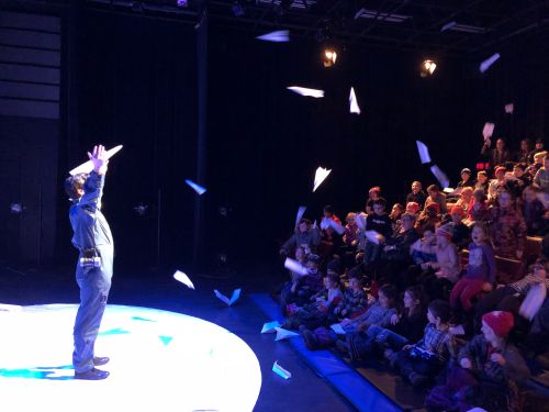 Photo of Richard Lam onstage with paper airplanes being thrown at him