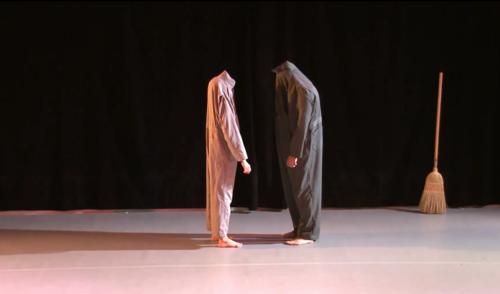 Photo of two dances facing each other wearing coveralls pulled up over their heads