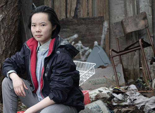 Photo of young adult sitting in front of pile of trash, promo photo for The Breath Between
