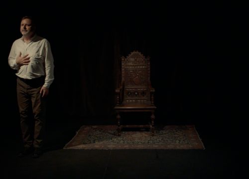 Justin Hay on a darkened stage next to a throne