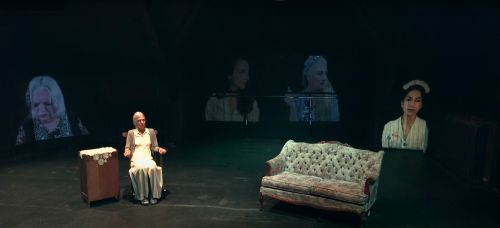 Anne Shepherd sitting in chair. Versions of herself at earlier ages are projected behind her 