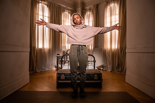 Natasha Mumba staing with arms outspread in front of a window